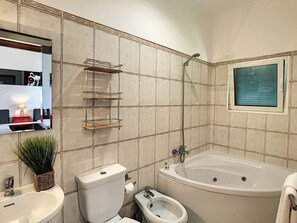 A bathroom with a toilet, bidet, sink, and bathtub. There is a mirror with a shelf above it, and a window with a view of the sea. - Villa Prainha by LovelyStay (Canical)