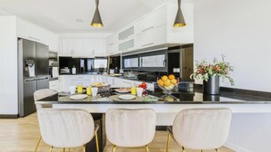 A modern kitchen with white cabinets, a central island, and three chairs with gold legs. - Villa Belmonte by Lovelystay (Ponta do Sol)