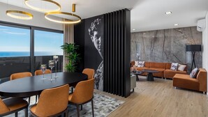 A modern living room with a large window, a black sofa, a coffee table, and a dining area with a table and chairs. - Villa Belmonte by Lovelystay (Ponta do Sol)