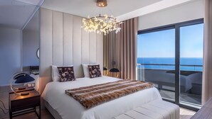 A modern hotel room with a large bed, a chandelier, a view of the ocean, and a balcony. - Villa Belmonte by Lovelystay (Ponta do Sol)