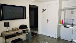 A modern kitchen with a built-in dishwasher, a flat-screen TV, and a small dining area with a glass table.