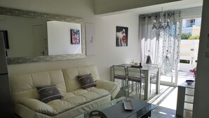 A modern living room with a beige sofa, a glass coffee table, and a dining area with a table and chairs.