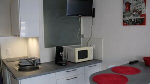 A compact kitchen with a microwave, coffee maker, and a flat-screen TV mounted on the wall. - Cozy Air-Conditioned Studio with Terrace & Parking, Ideal for 2 in Vibrant Agde (Cap d'Agde naturisme)