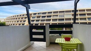 A balcony with a green chair and table, a black gate, and a building with multiple balconies in the background. - Cozy Air-Conditioned Studio with Terrace & Parking, Ideal for 2 in Vibrant Agde (Cap d'Agde naturisme)