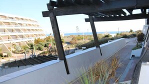 A modern building with a white facade and a wooden pergola overlooking a landscaped area with a view of the ocean. - Cozy Air-Conditioned Studio with Terrace & Parking, Ideal for 2 in Vibrant Agde (Cap d'Agde naturisme)