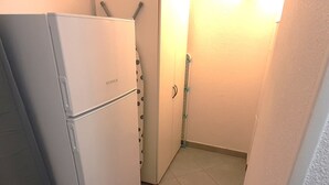 Uma cozinha compacta com uma geladeira branca, piso em azulejo e um corredor estreito.