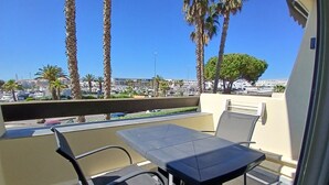 Varanda com mesa e cadeiras, vista para um estacionamento e edifícios.