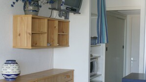 A wooden cabinet with drawers, a television mounted on the wall, and a door leading to a room. - Apartment for 4, equipped kitchen, terrace, parking, Cap d'Agde (Cap d'Agde naturisme)