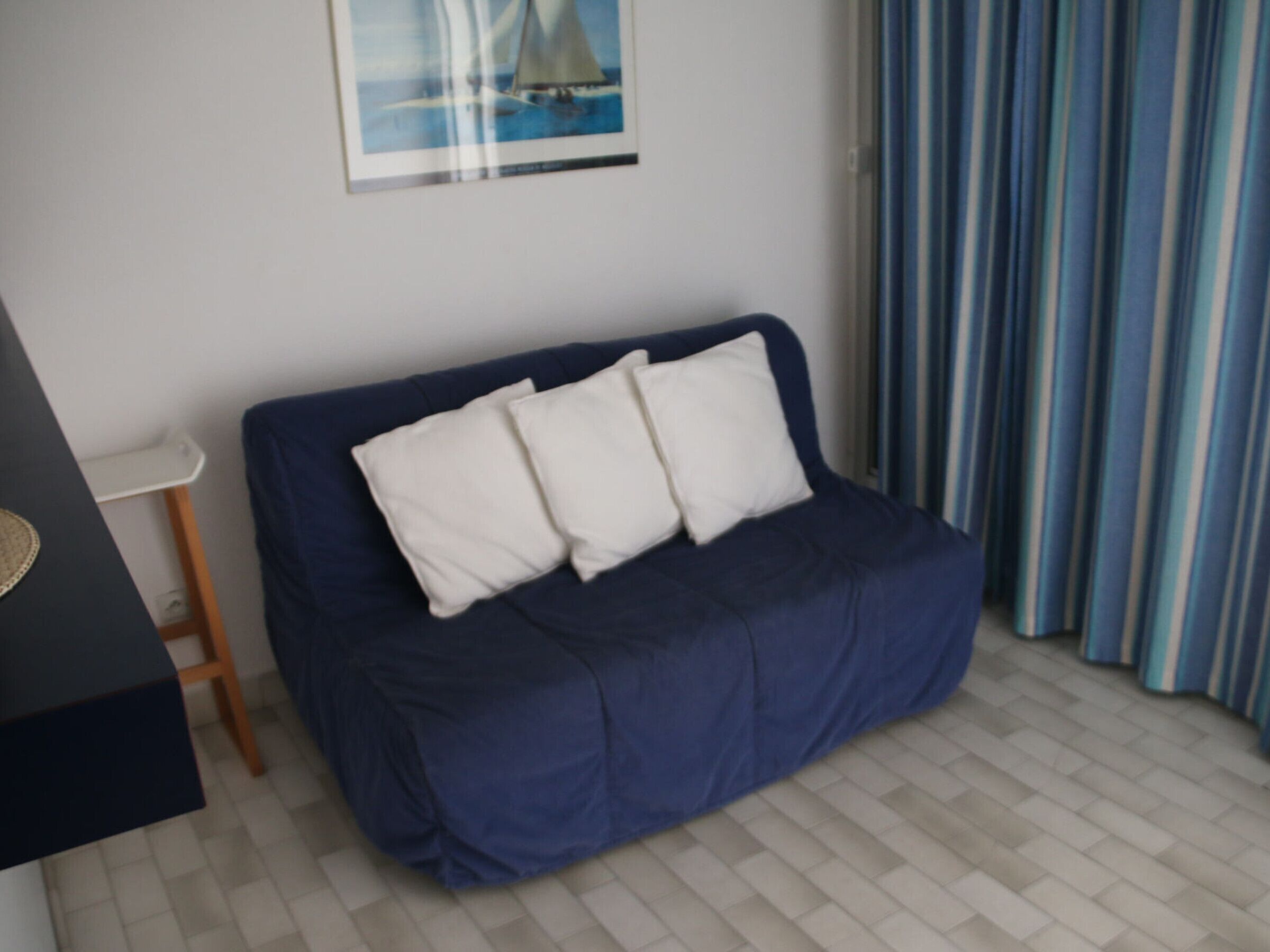 Une pièce avec un canapé bleu foncé, des coussins blancs, une petite table d’appoint en bois et un tableau encadré accroché au mur.