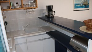 A kitchen with a sink, cabinets, a coffee maker, and a basket on the counter. - Apartment for 4, equipped kitchen, terrace, parking, Cap d'Agde (Cap d'Agde naturisme)