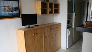 A kitchen with wooden cabinets, a microwave, and a television on a stand. - Apartment for 4, equipped kitchen, terrace, parking, Cap d'Agde (Cap d'Agde naturisme)