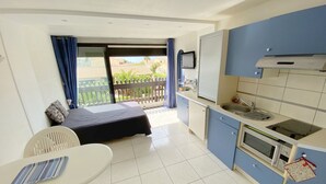 A compact room with a bed, a small table, a chair, a kitchenette, and a balcony with a view. - Cozy Studio with Pool Access, Port View, Parking Included - Agde (Cap d'Agde naturisme)
