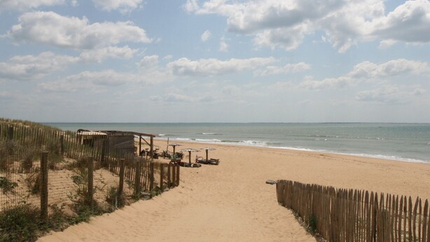 Une plage de sable avec une clôture en bois et des chaises de plage.
