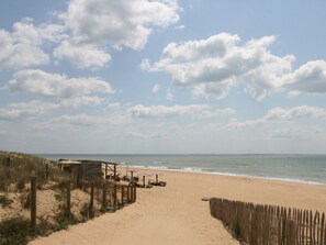 A sandy beach with a wooden fence and beach chairs.