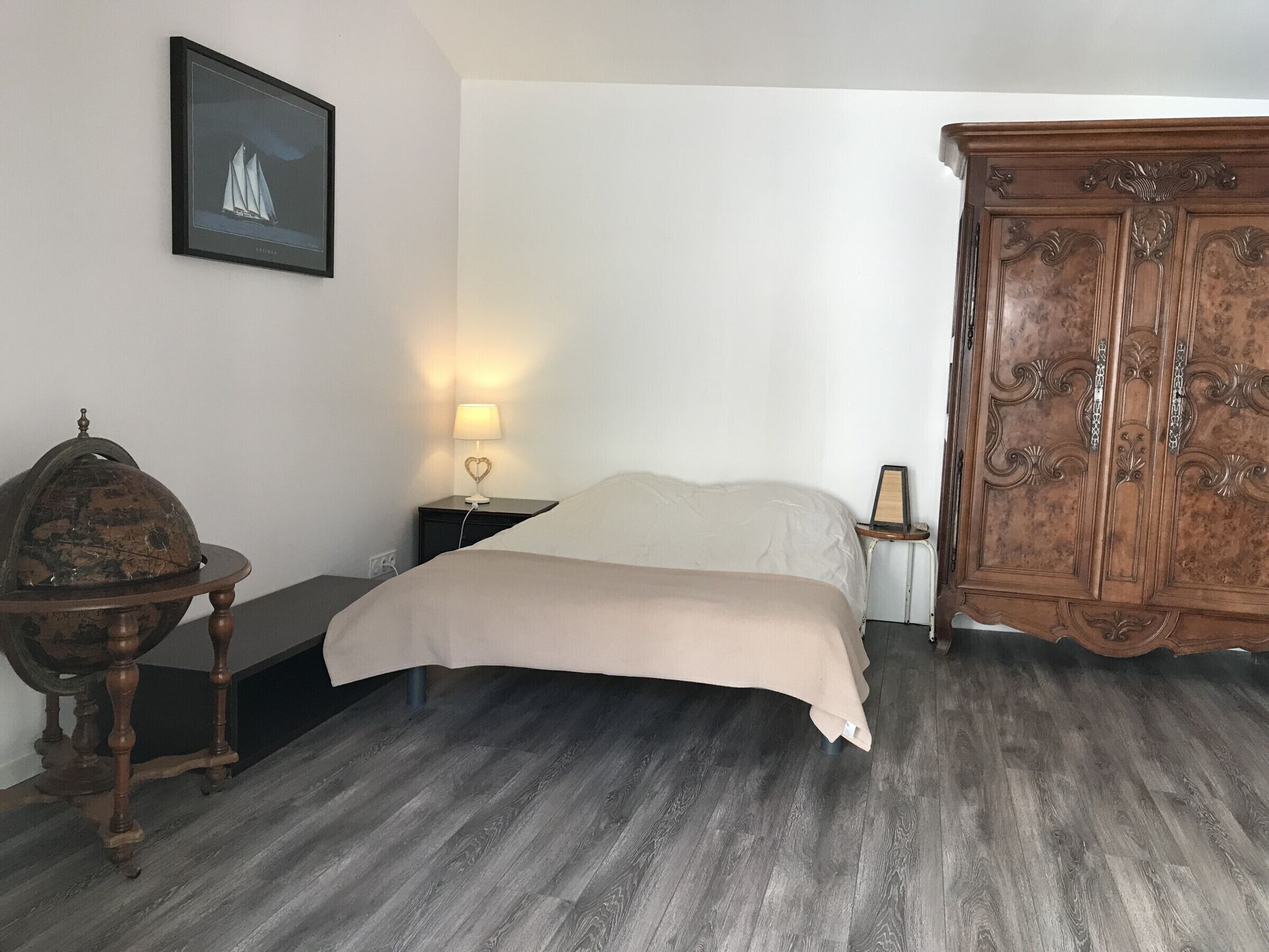 Een slaapkamer met een bed, een nachtkastje met een lamp, een houten kast en een lijst met een afbeelding aan de muur.