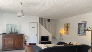 Un salon avec un meuble en bois, un canapé noir, une petite table, une lampe et un escalier.