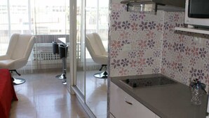 Ett modernt kök med mikrovågsugn, diskho och kakelbeklädd vägg bakom arbetsbänken. I det intilliggande området finns det två stolar och ett bord.