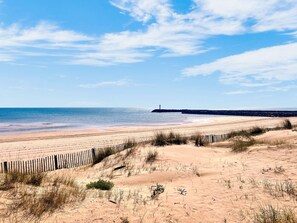 A beach with a wooden fence, sandy dunes, and a lighthouse in the distance. - Air-conditioned studio with parking and WiFi in Cap d'Agde (Cap d'Agde naturisme)