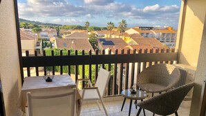 A balcony with a table and chairs, a wicker chair, and a view of buildings and trees. - Charming Studio with Pool Access, Terrace, and Parking in Agde (Cap d'Agde naturisme)