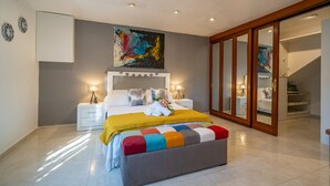 Een moderne slaapkamer met een groot bed, nachtlampjes, een kleurrijke bank en een schuifdeurkast.