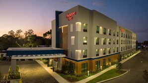 Un hôtel Hampton Inn au design moderne, doté d’une entrée bien éclairée et d’un espace de stationnement.