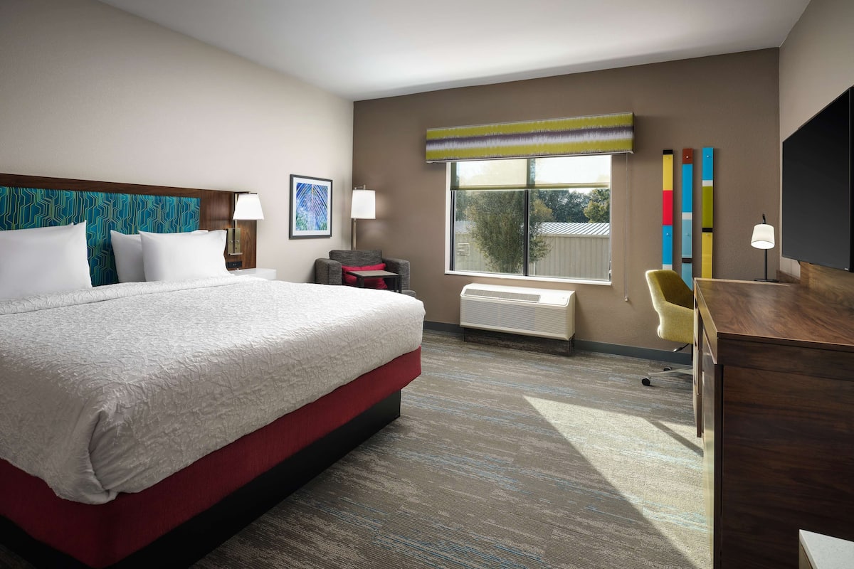 A hotel room with a large bed, a desk, a chair, a window, and a radiator.