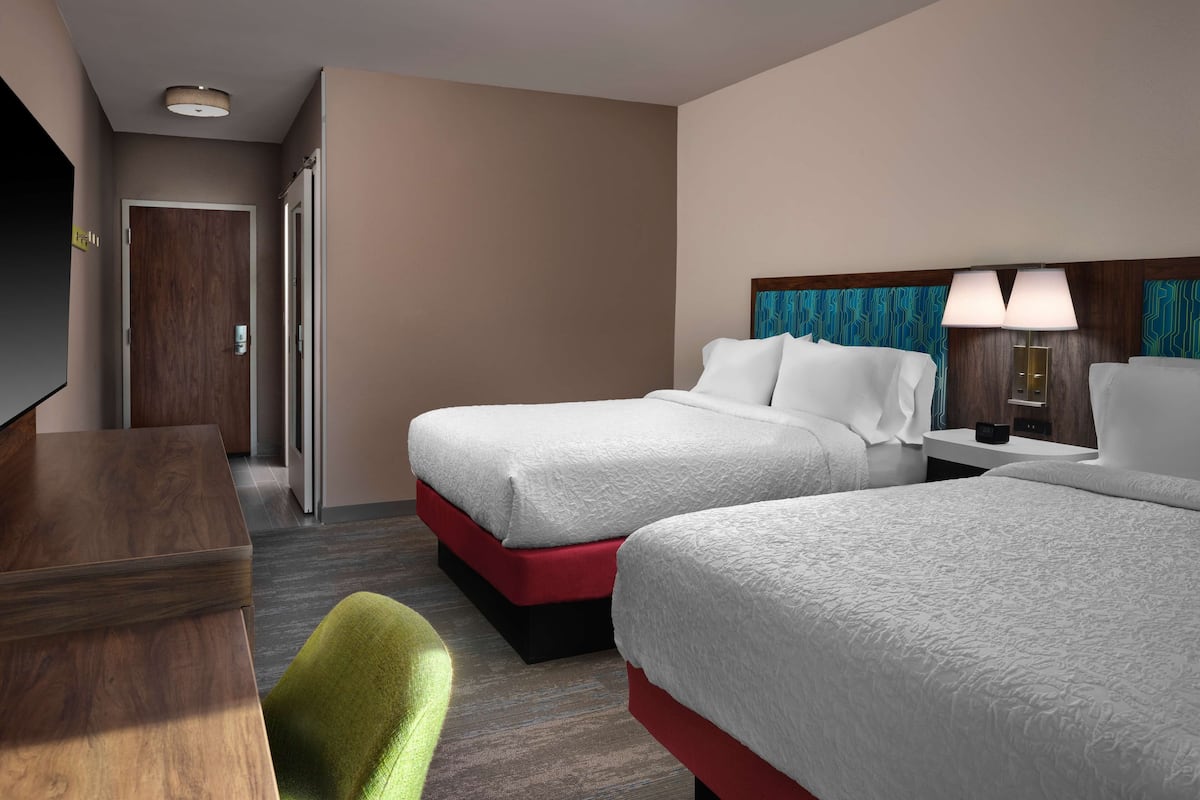A hotel room with two beds, a desk, a television, and a door.