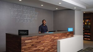 Un comptoir d’accueil d’hôtel avec un panneau décoratif en bois, une enseigne indiquant « Hilton Honors » et une citation inspirante affichée sur le mur.
