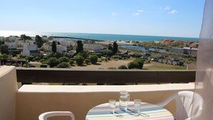 A balcony with a table set for two, overlooking a coastal area with buildings and a beach.