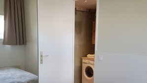 Une petite pièce, de taille modeste, comprenant un lave-linge, un lit recouvert d’une courtepointe à motifs floraux et une porte donnant sur une autre pièce.