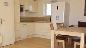 Une cuisine compacte avec des meubles blancs, un four à micro-ondes et un petit réfrigérateur. On y trouve une table à manger en bois avec des chaises.