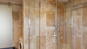 Une douche fermée par des parois en verre, dotée d’un pommeau de douche à main et d’un flexible de douche à main.