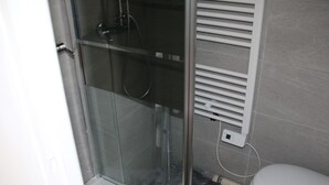 Un bagno con box doccia in vetro, un water bianco e un termosifone a parete.