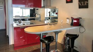 A modern kitchen with red cabinets, a bar area with stools, and a coffee machine. - Air-conditioned studio with pool, parking, wifi - Cap d'Agde (Cap d'Agde naturisme)