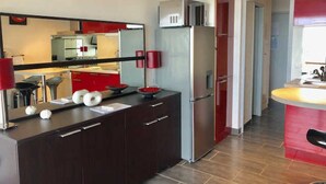 A modern kitchen with dark cabinetry, a stainless steel refrigerator, and a red accent wall. - Air-conditioned studio with pool, parking, wifi - Cap d'Agde (Cap d'Agde naturisme)