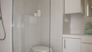 Kylpyhuoneessa on lasiseinällä varustettu suihku, wc ja pesuallas, jonka yläpuolella on kaappi.