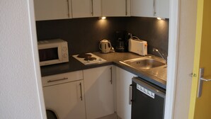 Ett kompakt kök med vita skåp, en mikrovågsugn, en brödrost, en kaffebryggare och ett handfat.