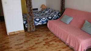 Ett sovrum med trägolv, en säng med ett mönstrat överkast, en rosa soffa med kuddar och en dörr som leder till ett annat rum.