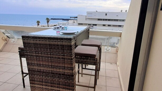 Un balcón con una mesa de mimbre y dos taburetes altos, con vista al mar.