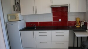 Una cocina compacta con armarios blancos, encimera negra y salpicadero con azulejos rojos.