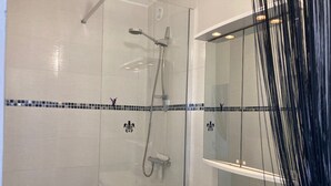 Un baño con cabina de ducha de vidrio, un lavamanos blanco con espejo y salpicadero de azulejos.
