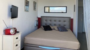 Un dormitorio con cama, televisor, tetera roja y ventana con vistas.