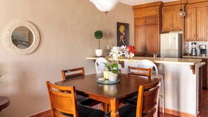 Un comedor con una mesa y sillas de madera, una lámpara colgante y una cocina con armarios y electrodomésticos de madera.