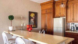 Una cocina con gabinetes de madera, un refrigerador de acero inoxidable, un lavamanos blanco y un taburete de bar.