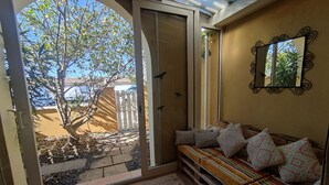 Quarto com porta de vidro deslizante para área externa, um banco de madeira e uma pequena mesa com um livro.