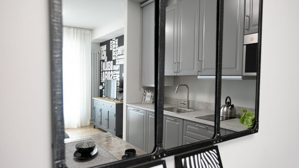 A modern kitchen with grey cabinets, a black-framed mirror, and a stainless steel kettle on the counter. - Urban Zebra Modern Studio in Donizetti Residence (Bergamo)