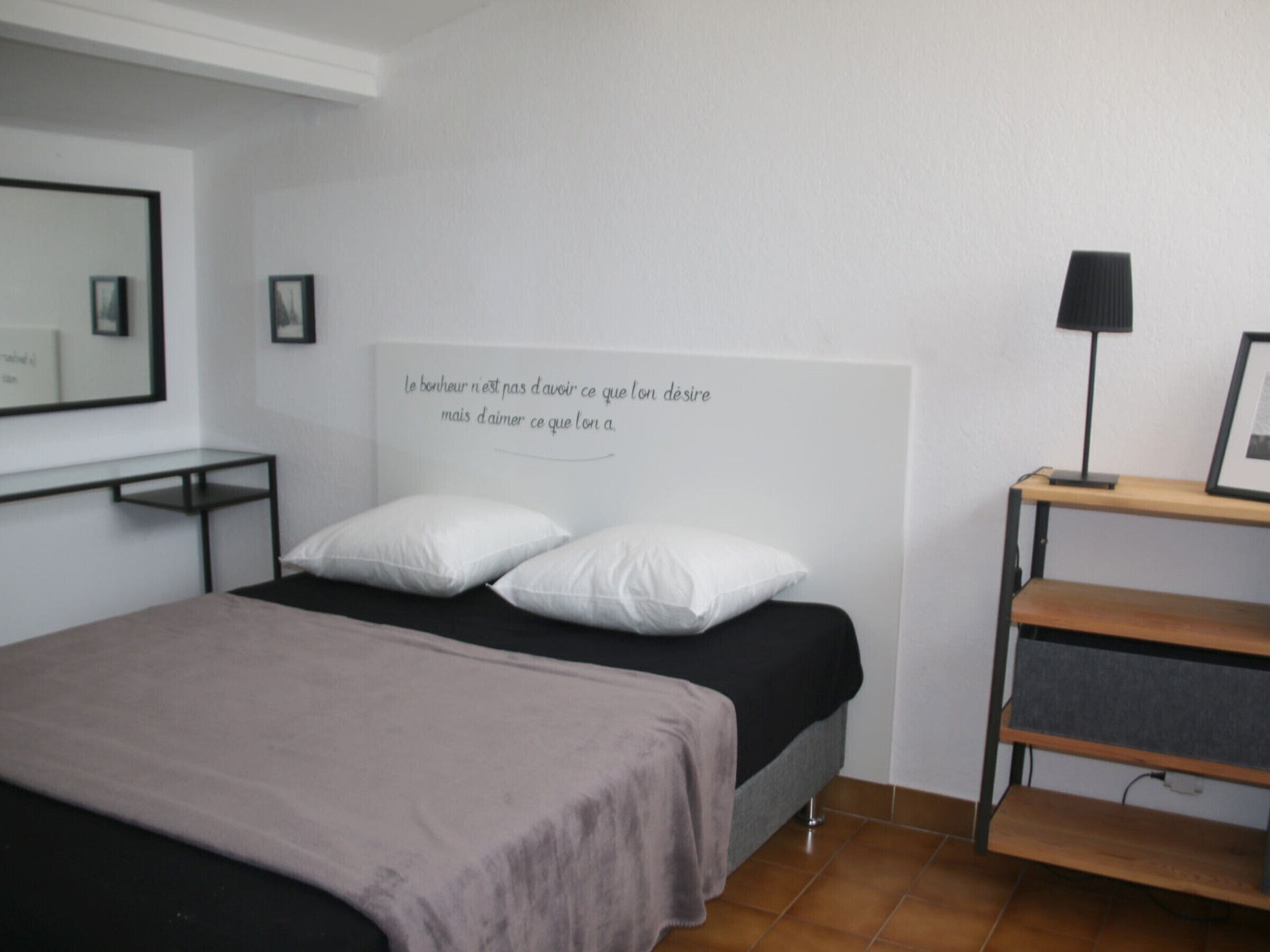 Un dormitorio con una cama, dos almohadas, una mesita de noche, una lámpara y un estante en la pared.
