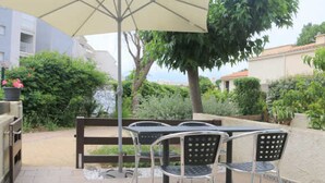 An outdoor patio with a table and chairs, a large umbrella, and a grill. - Charming Villa in Agde: 2BR, A/C, Private Terrace, WiFi, Parking (Cap d'Agde naturisme)