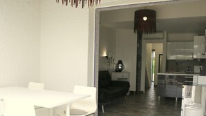 A modern kitchen with white cabinets and a dining area with a white table and chairs. - Charming Villa in Agde: 2BR, A/C, Private Terrace, WiFi, Parking (Cap d'Agde naturisme)