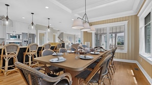 A spacious dining area with a long wooden table, wicker chairs, and modern pendant lighting. - Happy Holidays with Sea Breeze (Scarborough)